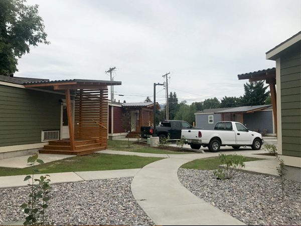 A photograph of four manufactured homes surrounding a courtyard where two pickup trucks are parked.